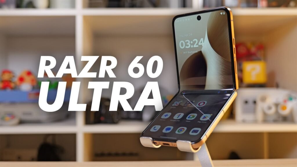 Motorola Razr 60 Ultra, uno smartphone pieghevole posizionato su un supporto da tavolo. Il dispositivo è aperto a L, evidenziando sia il display interno, che mostra l'orario (03:24), la data (giovedì 24 aprile) e la posizione (Bucarest), sia la schermata home con le app principali in basso.

Il design del telefono appare raffinato e moderno, con cornici sottili e un corpo dorato. Sullo sfondo sfocato si intravede una libreria con giocattoli, una console e oggetti geek/retro, creando un contesto domestico e tech-friendly.