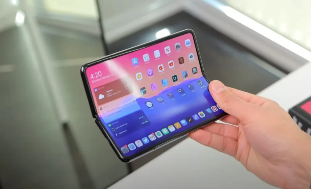 iPhone Pieghevole: Il Futuro della Mobilità Intelligente Un prototipo di smartphone pieghevole con interfaccia iOS mostrato in uso, che evidenzia la versatilità di un display flessibile e la possibilità di avere uno schermo più ampio in un dispositivo tascabile. La mano che lo regge suggerisce le dimensioni compatte nonostante l'ampio display.